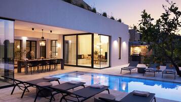 A modern house with a swimming pool, outdoor seating, and a dining area.