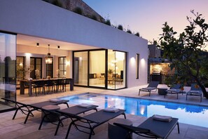 A modern house with a swimming pool, outdoor seating, and a dining area. - Citrus Grove Luxury Villas (Rethymno)