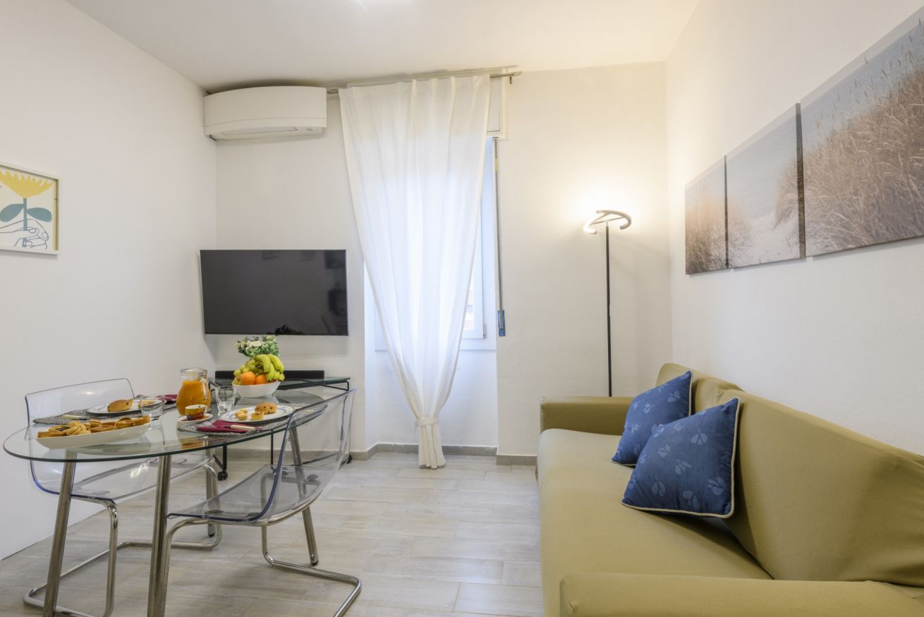A compact living space with a dining area, a sofa, a flat-screen TV, and artwork on the walls.