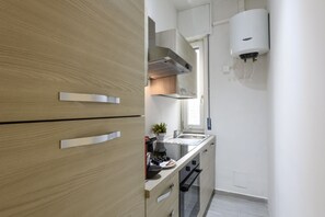 A compact kitchen with wooden cabinets, a built-in oven, and a wall-mounted water heater. - Monte Ceneri, 71 - Modern, convenient and well-connected (Milan)
