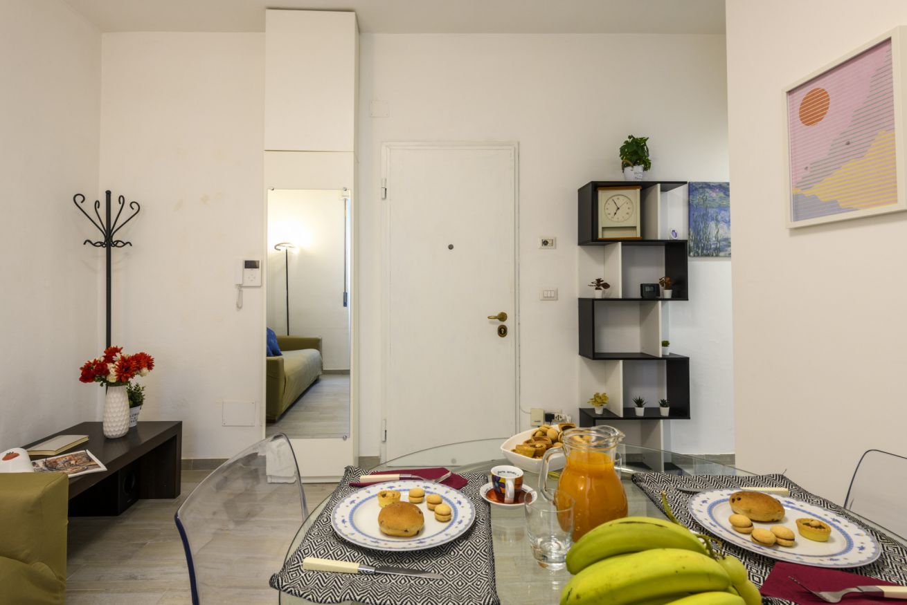 A dining area with a table set for breakfast, a clock on the wall, and a door leading to another room.