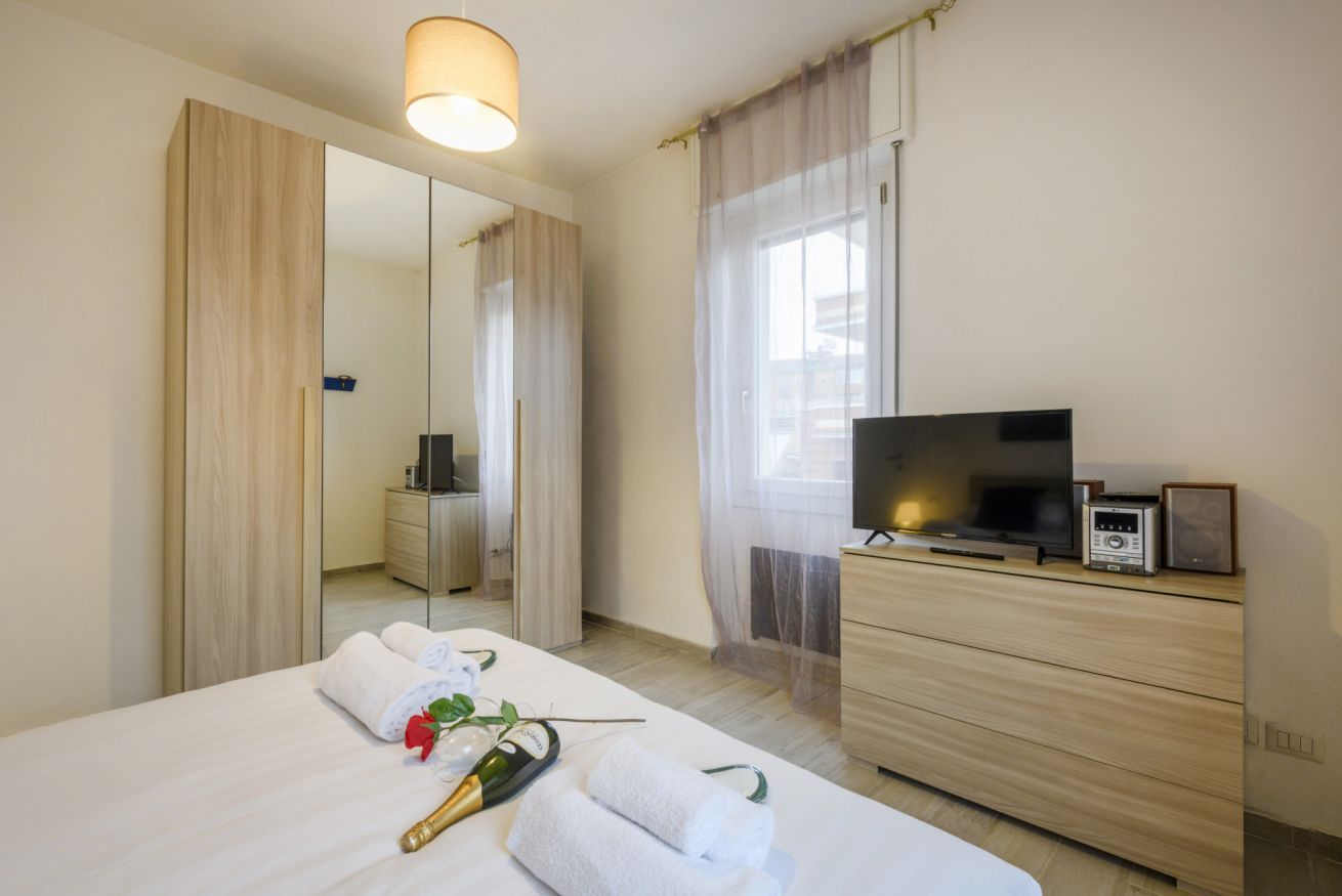 A hotel room with a bed, a TV, a dresser, a mirror, and a window with curtains.