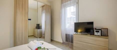 A hotel room with a bed, a TV, a dresser, a mirror, and a window with curtains.
