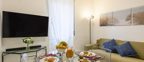 Ein Wohnzimmer mit Glastisch, einer Couch, einem Flachbildfernseher und einem Gemälde an der Wand.