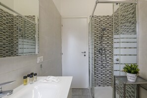 A bathroom with a white sink, a glass shower enclosure, and a potted plant on a small table. - Monte Ceneri, 71 — Modern, practical, and well-connected (Milan)