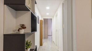 A hallway with a plant on a shelf, a clock, and a door at the end. - Monte Ceneri, 71 - Modern, convenient and well-connected (Milan)