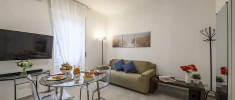 Uma sala de estar moderna com um sofá, uma mesa de jantar de vidro e uma televisão de tela plana.