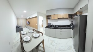 Eine moderne Küche mit Einbaukühlschrank, ein Essbereich mit Tisch für vier Personen und ein Wohnbereich mit Sofa und Fernseher.
