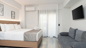 Ein modernes Hotelzimmer mit Bett, grauem Sofa, Flachbildfernseher und Kunstwerken an den Wänden.