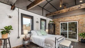 A bedroom with a bed, a nightstand, a dresser, a large window, and a sliding glass door leading to a balcony. - Luxury Renovated Barn Near Bennett Springs – Cozy & Private (Lebanon)