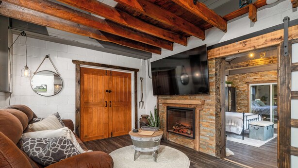 A living room with a leather sofa, a round coffee table, a fireplace, and a television mounted on the wall. - Luxury Renovated Barn Near Bennett Springs – Cozy & Private (Lebanon)