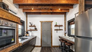 A kitchen with a built-in oven, a stainless steel refrigerator, wooden beams, and a door with a small window. - Luxury Renovated Barn Near Bennett Springs – Cozy & Private (Lebanon)