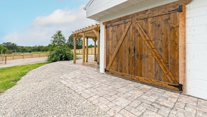 A building with a large wooden garage door, a covered patio area, and a gravel pathway. - Luxury Renovated Barn Near Bennett Springs – Cozy & Private (Lebanon)