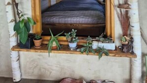 Una habitación acogedora con techo de madera, una ventana con marco de madera y una cama con cubierta oscura. Hay plantas en macetas en el alféizar.