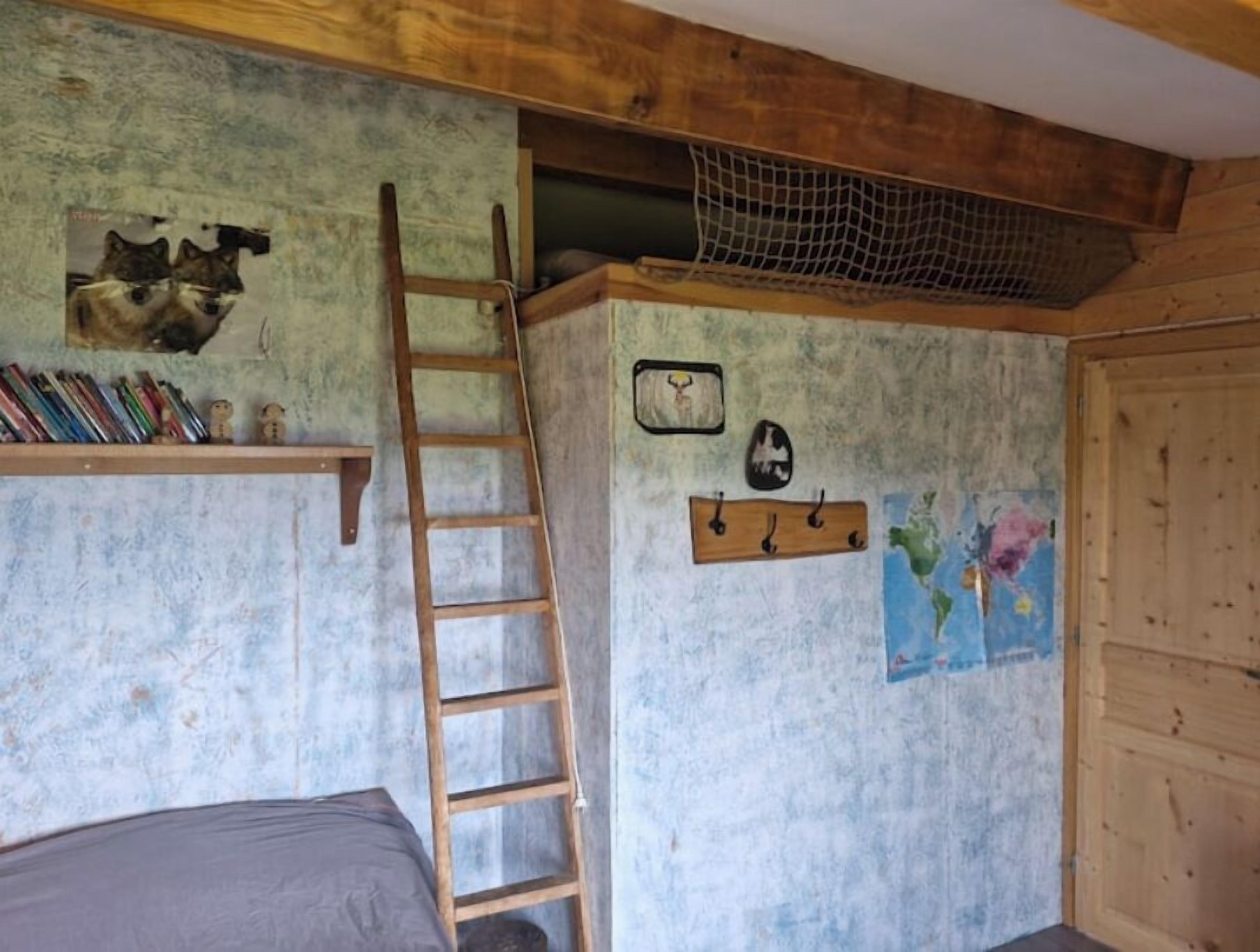 Una habitación rústica con una escalera de madera, un estante con libros, un reloj de pared y un mapa.