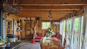 Interior de una cabaña de madera con una mesa de comedor, sillas, un sofá y un ventanal grande.