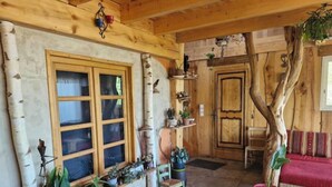 Interior acogedor de una cabaña con un ventanal grande, paredes de madera, chimenea y diversas plantas en macetas.