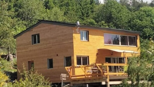 Una casa de madera de dos pisos con un balcón, rodeada de abundante vegetación.