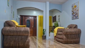 Una sala de estar con dos sofás marrones, una puerta de madera, una cortina amarilla y una planta en maceta.