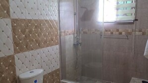 Un baño con ducha, inodoro y pared de azulejos.