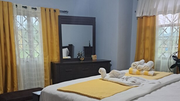 Habitación de hotel con dos camas, un aparador de madera oscura, un espejo y una ventana con cortinas amarillas.