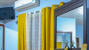 Una habitación con un aparador de madera, un otomano marrón, un espejo y un aire acondicionado instalado en el techo.