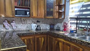 Una cocina con armarios de madera, encimera de granito, microondas, cafetera y lavabo.