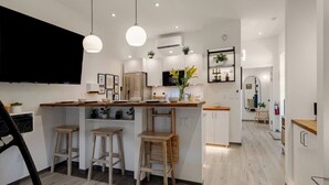 Una cucina moderna con isola centrale, sgabelli da bar, illuminazione a sospensione e una TV a schermo piatto.
