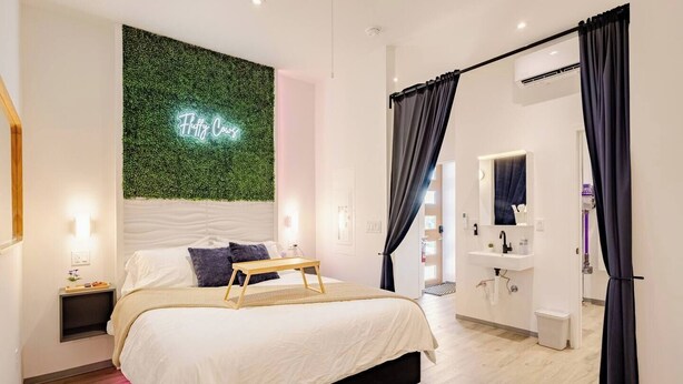 Una camera da letto moderna con un letto, comodini, un neon e un bagno con specchio e lavandino.