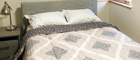 A bedroom with a bed, a nightstand, a lamp, and a window with blinds.