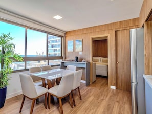 A modern kitchen with a dining area, wooden flooring, and large windows offering a city view. - 2 suites on a high floor in Barra with ocean view (Salvador)