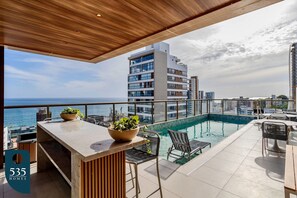 A rooftop pool area with a bar, seating, and a view of the sea. - 2 suites on a high floor in Barra with ocean view (Salvador)