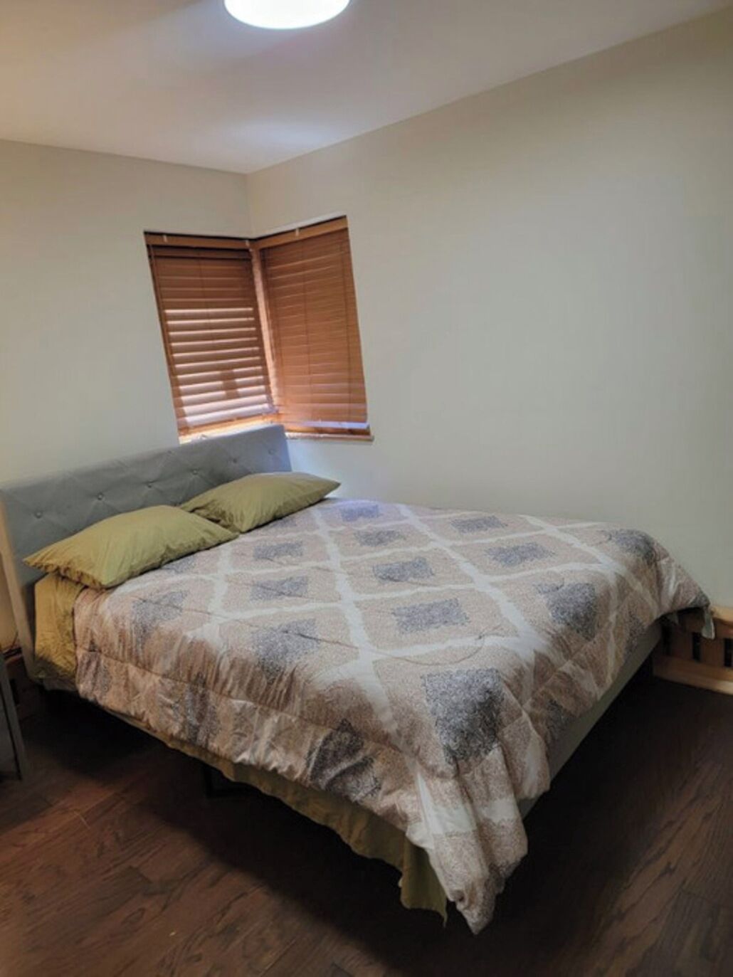 A bedroom with a bed, wooden floor, and a window with blinds.