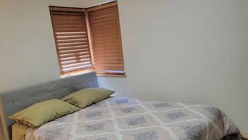 A bedroom with a bed, wooden floor, and a window with blinds.