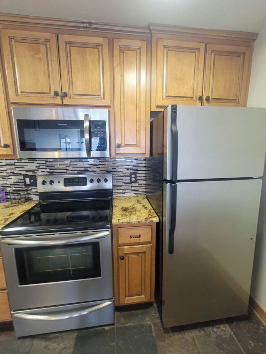 A kitchen with wooden cabinets, a stainless steel refrigerator, a microwave, and an oven.