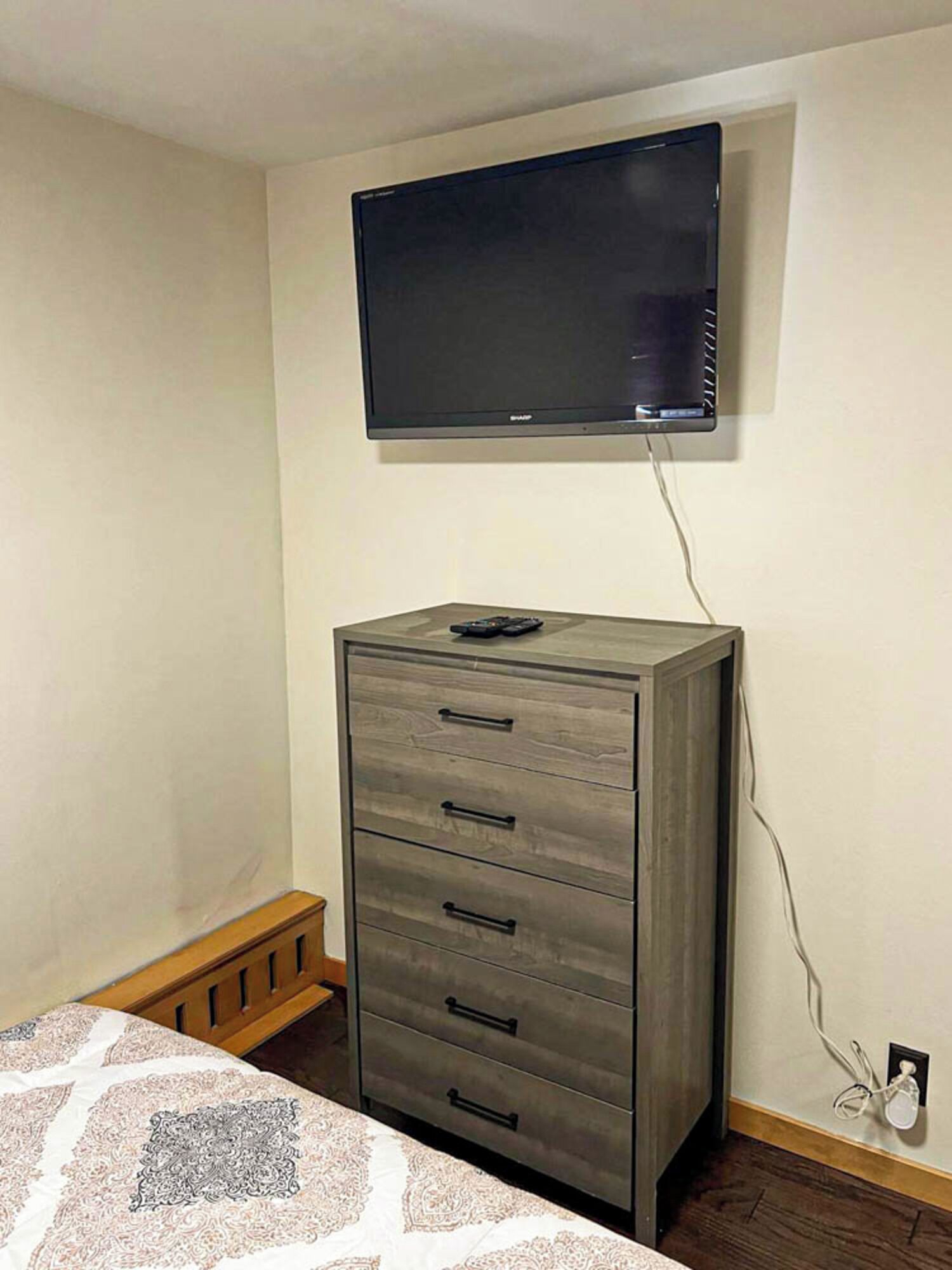 A bedroom with a bed, a dresser, a television mounted on the wall, and a power outlet on the wall.