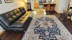 Un salon avec un canapé en cuir, une table basse en verre et un tapis à motifs.
