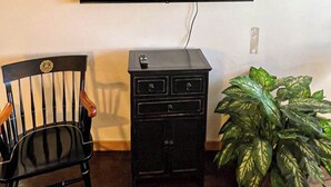 Un téléviseur à écran plat fixé au mur, un petit meuble noir en dessous, une chaise en bois et une plante en pot.
