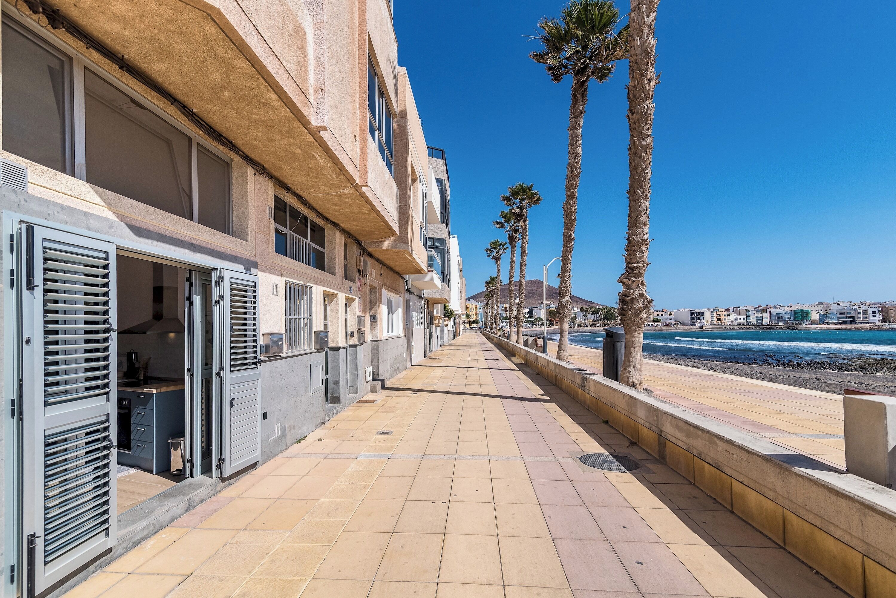 A coastal walkway with buildings, palm trees, and a view of the sea.