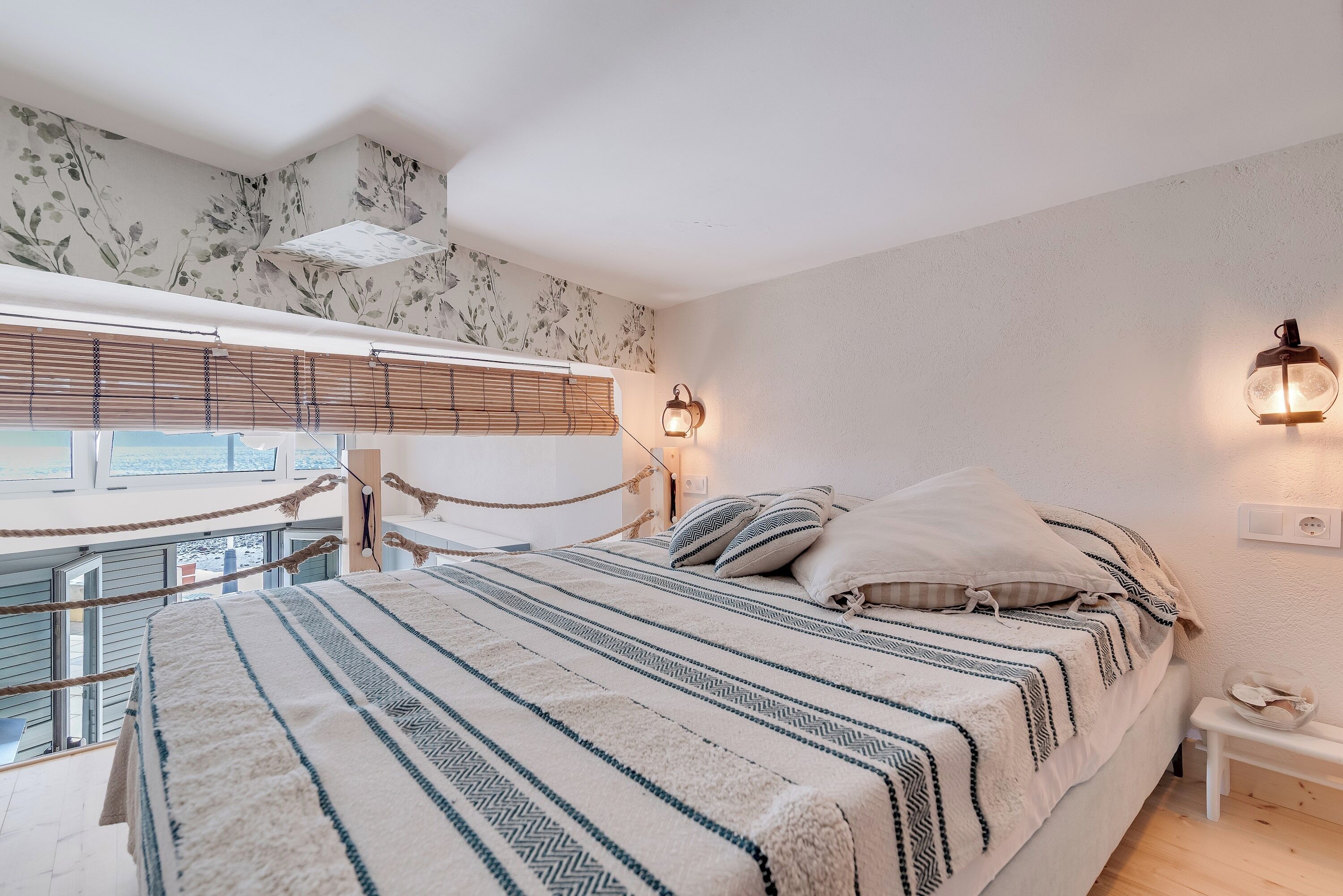 Un dormitorio con una cama, una mesita de noche, una lámpara de pared y una ventana con persianas.
