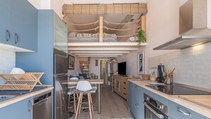 Een kleine keuken met moderne apparatuur, een eethoek met krukken, en een slaapverdieping met een bed.