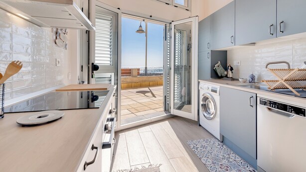 Een moderne keuken met een wasmachine, een eethoek en uitzicht op zee.