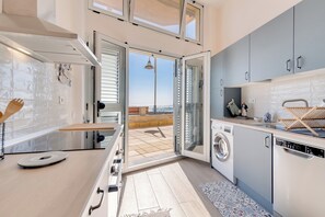 A modern kitchen with a washing machine, a dining area, and a view of the sea. - Home2Book El Camarote Seafront Retreat in Arinaga (Arinaga)
