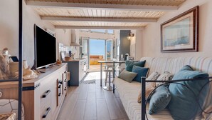 Een knus interieur met een houten plafond, een bank met kussens, een televisie en een eethoek met een tafel en stoelen.