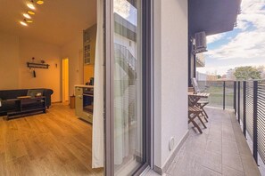 Ein offener Wohnbereich mit einer Schiebetür, die auf einen Balkon mit Blick auf ein Gebäude und Bäume führt.