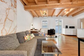 Ein Wohnzimmer mit einer Couch, einem Couchtisch, einem Fernseher und einer Küchenzeile im Hintergrund.