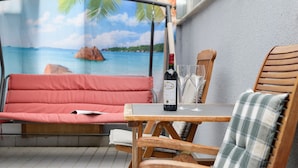 Una habitación con una cama tapizada de rojo, una mesa de madera con una botella de vino y copas, y un mural con una escena de playa tropical.