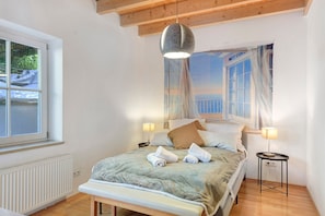 A bedroom with a bed, two bedside lamps, a window, a radiator, and a wooden ceiling.