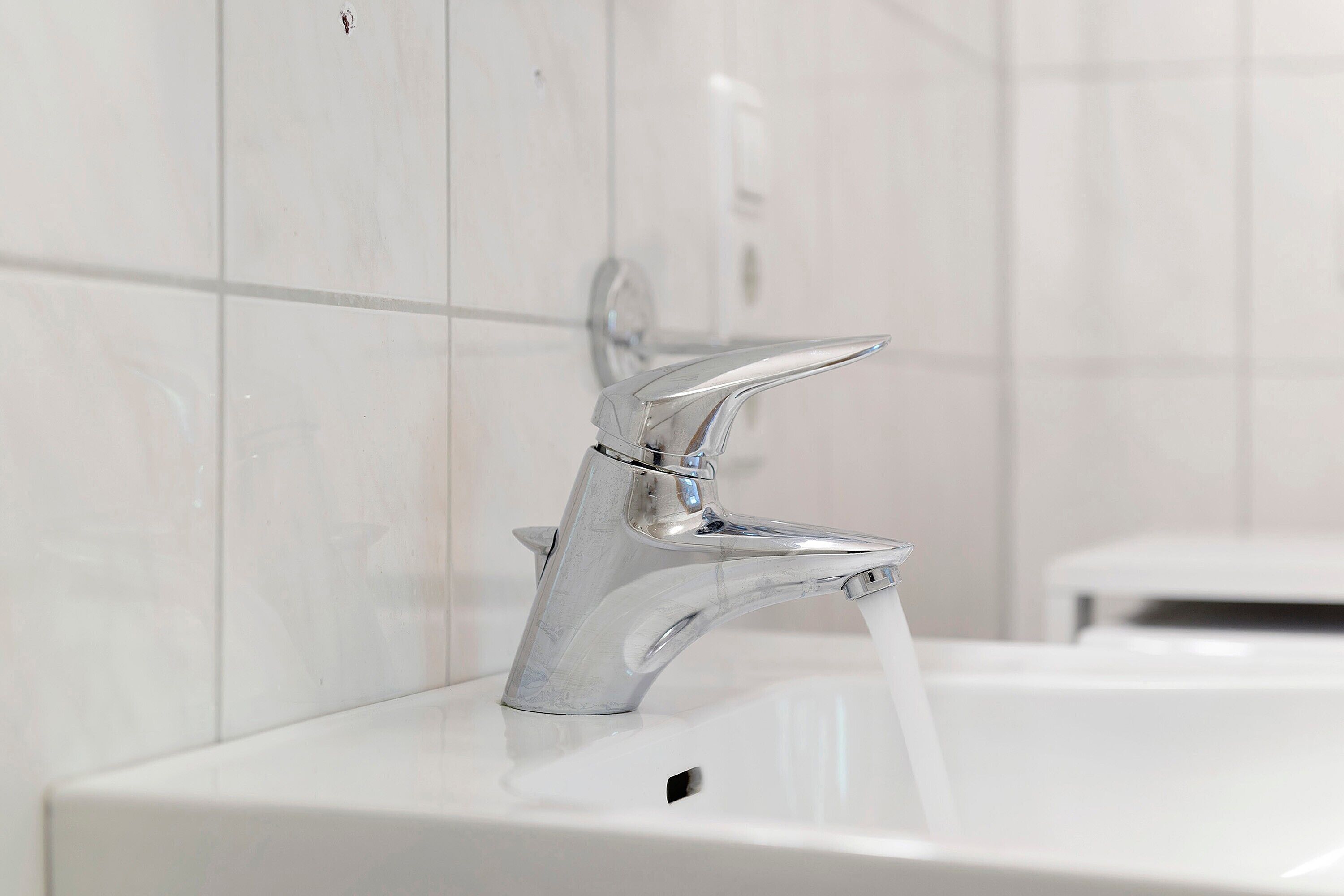 A modern bathroom with a chrome faucet, a white sink, and a tiled wall.