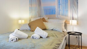 Una cama bien hecha con toallas enrolladas, una lámpara de noche y vistas al balcón por la ventana.